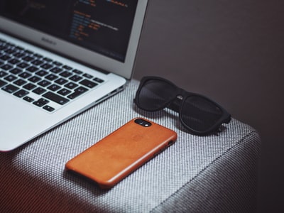 橙智能手机附近的黑框太阳镜MacBook Air旁边
